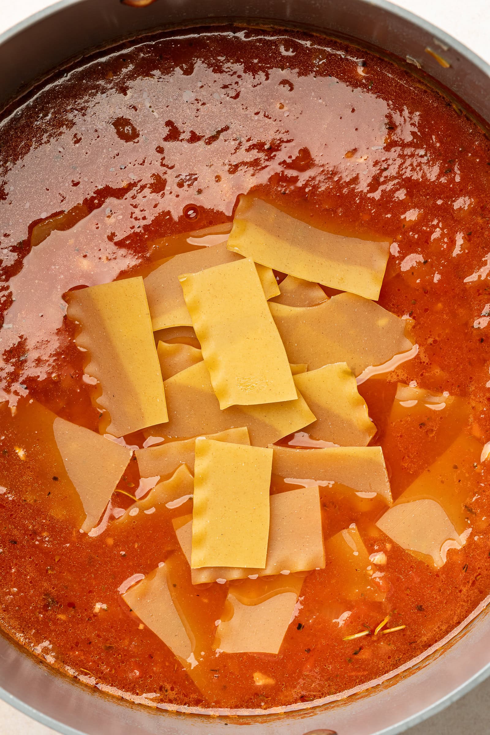 Dry and broken up lasagna noodles being added to large soup pot of soup.