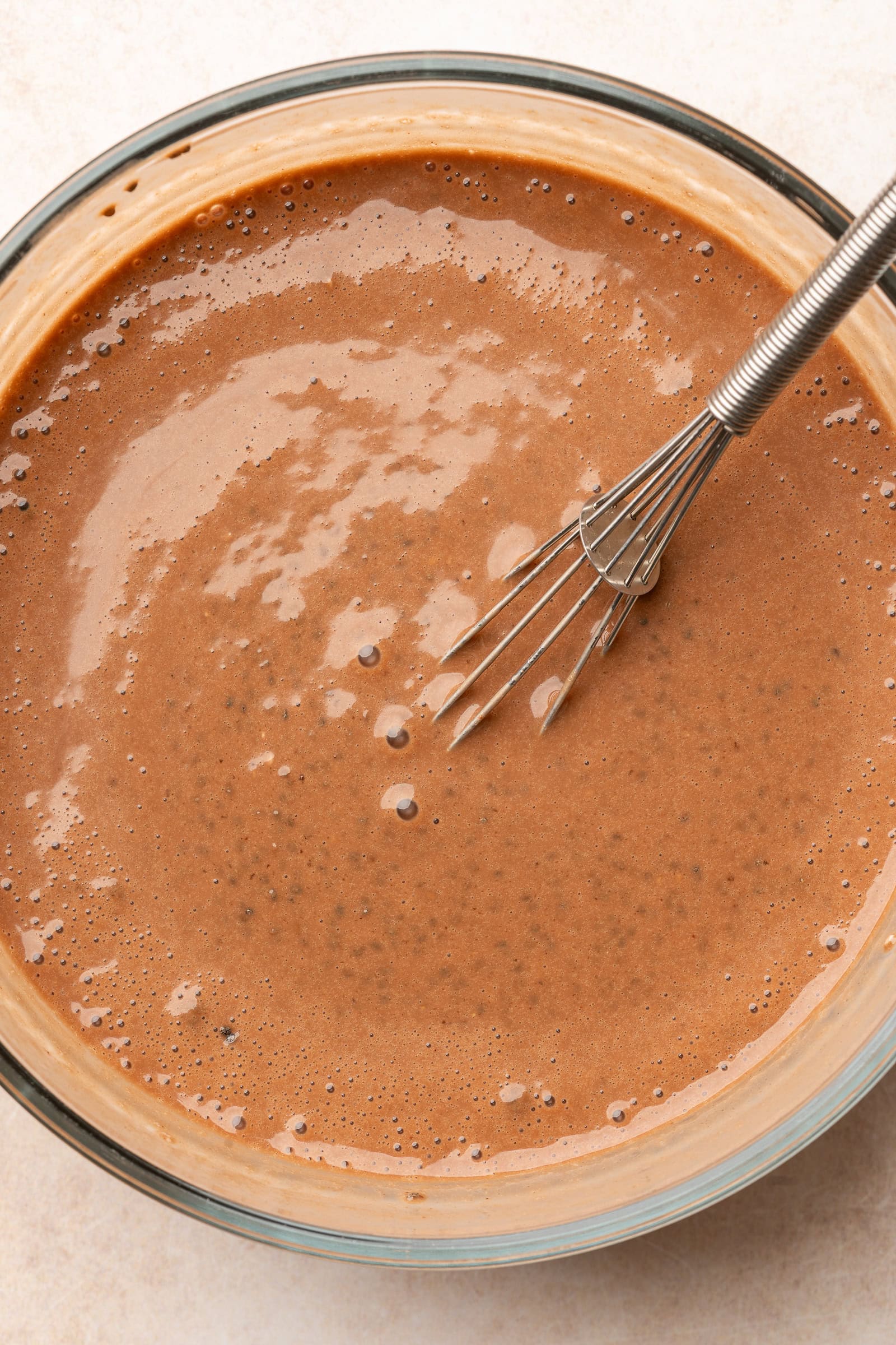 Chocolate banana milk being whisked with chia seeds in a glass bowl.