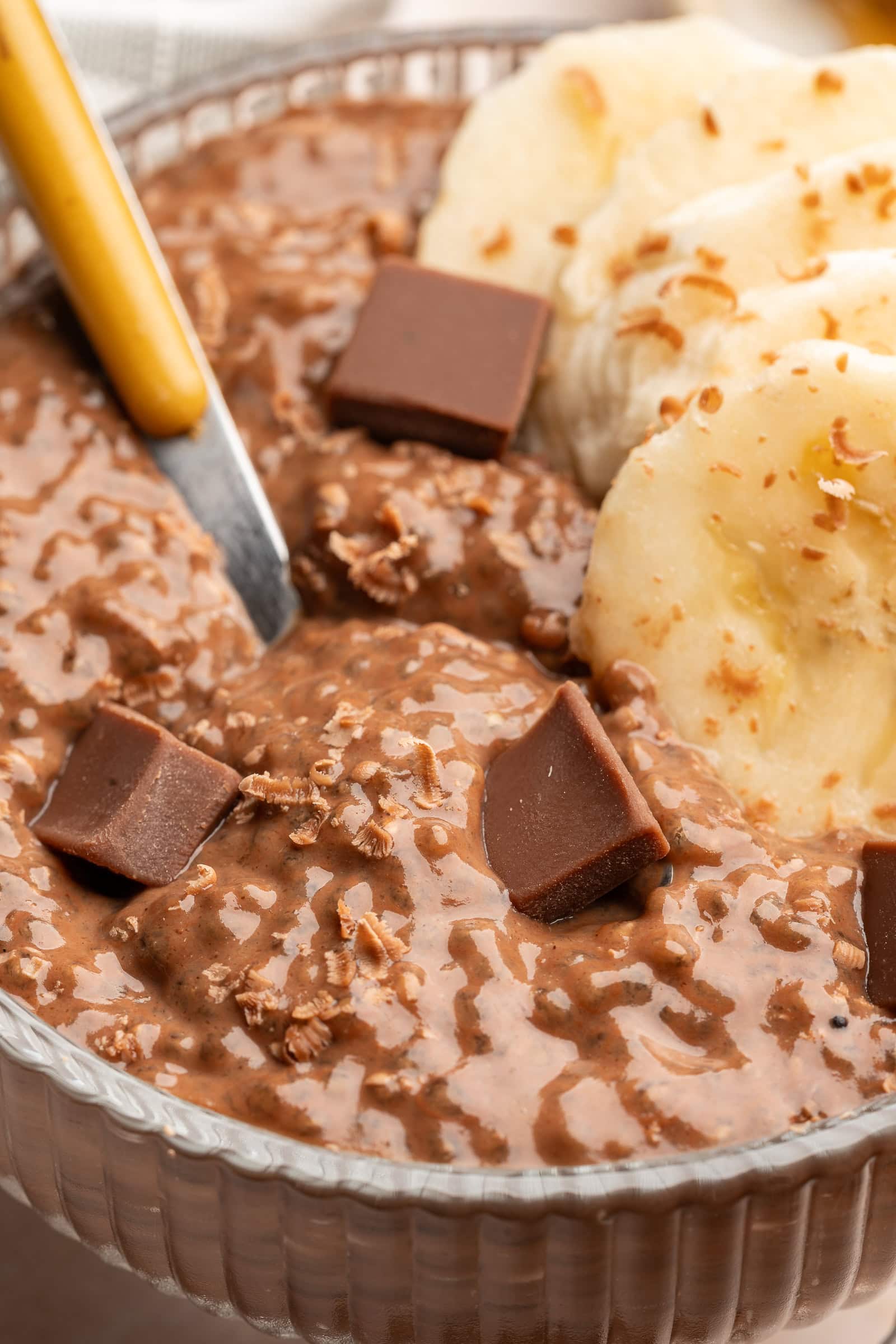 Close up of chocolate banana pudding in a glass serving bowl topped with chocolate shavings and banana slices.