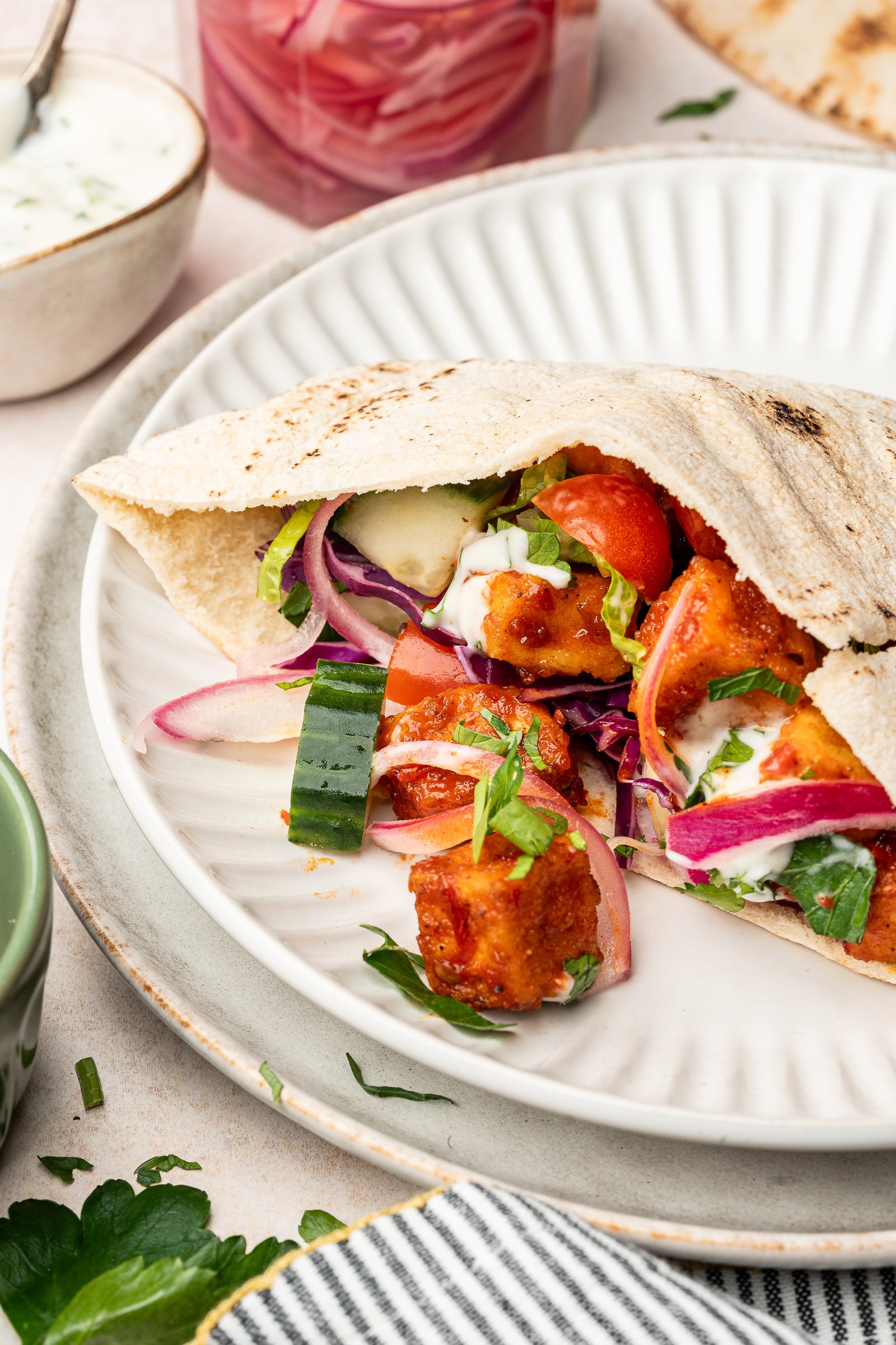 Harissa tofu stuffed in a pita with cucumbers, red onions, lettuce, and parsley.