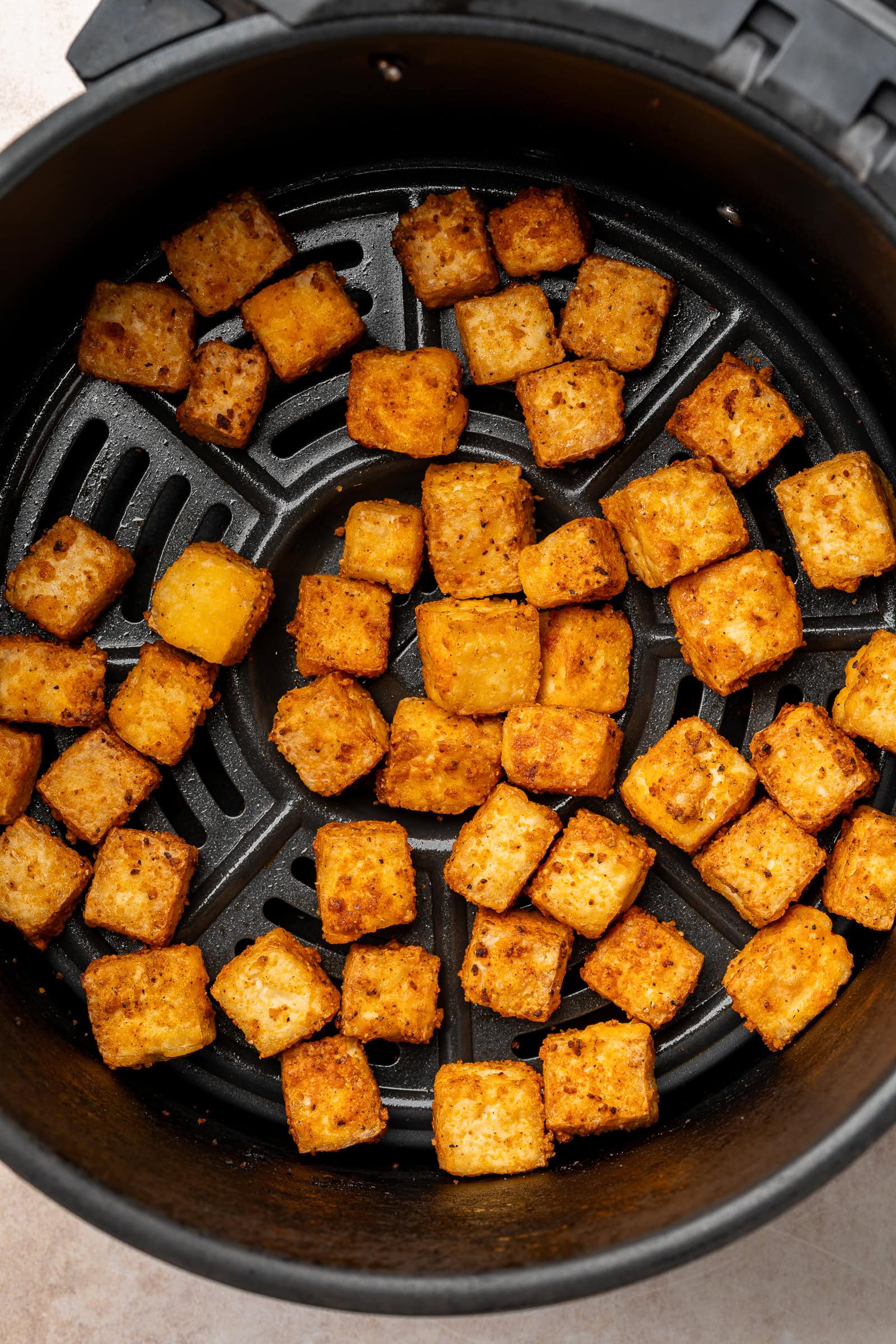 Crispy tofu cubes in air fryer basket.