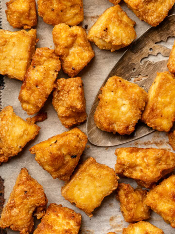 Crispy baked tofu on parchment lined baking sheet with spatula.