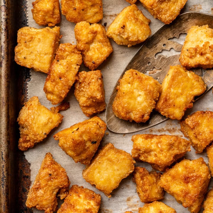 Crispy baked tofu on parchment lined baking sheet with spatula.