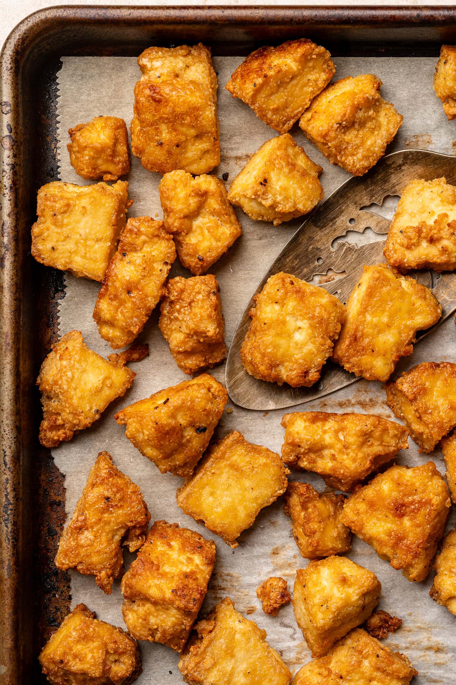 Crispy baked tofu on parchment lined baking sheet with spatula.