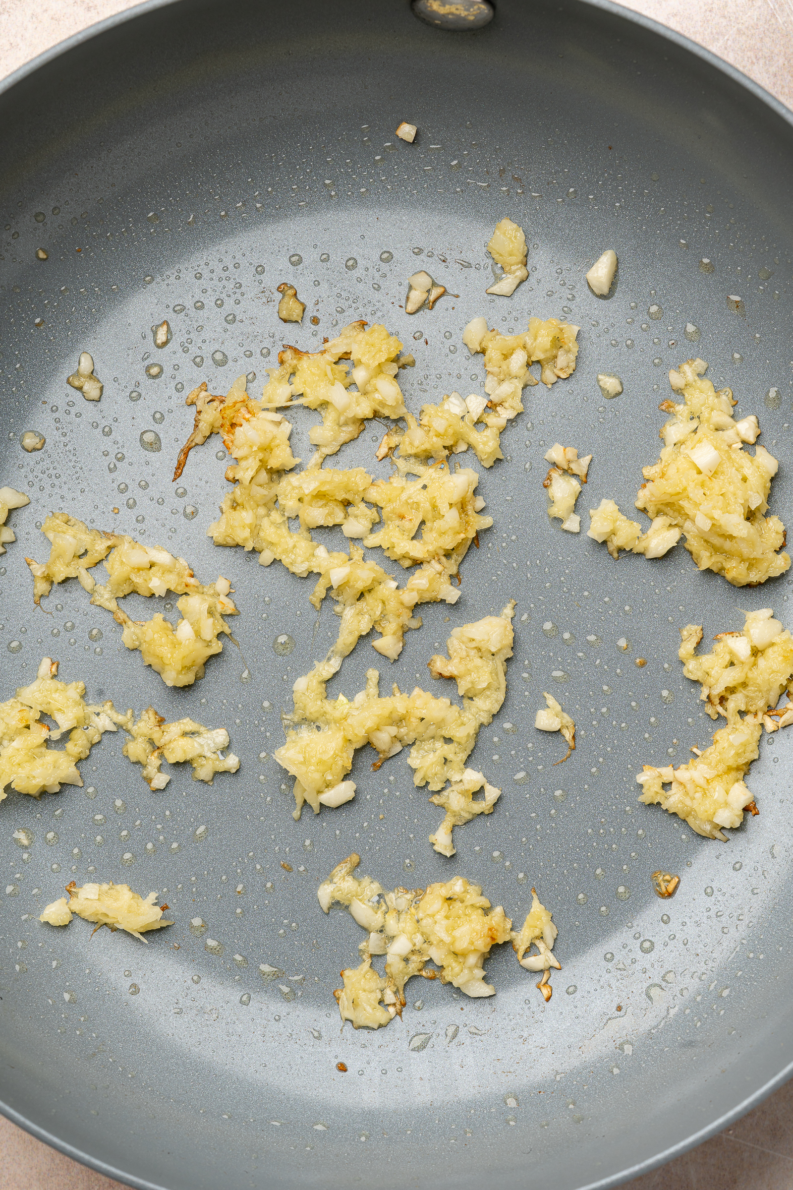 Garlic and ginger being cooked in oil in a frying pan.