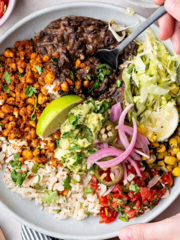 Vegan tofu burrito bowl with black beans, tofu crumbles, corn, pico de gallo, guacamole, and lime wedges