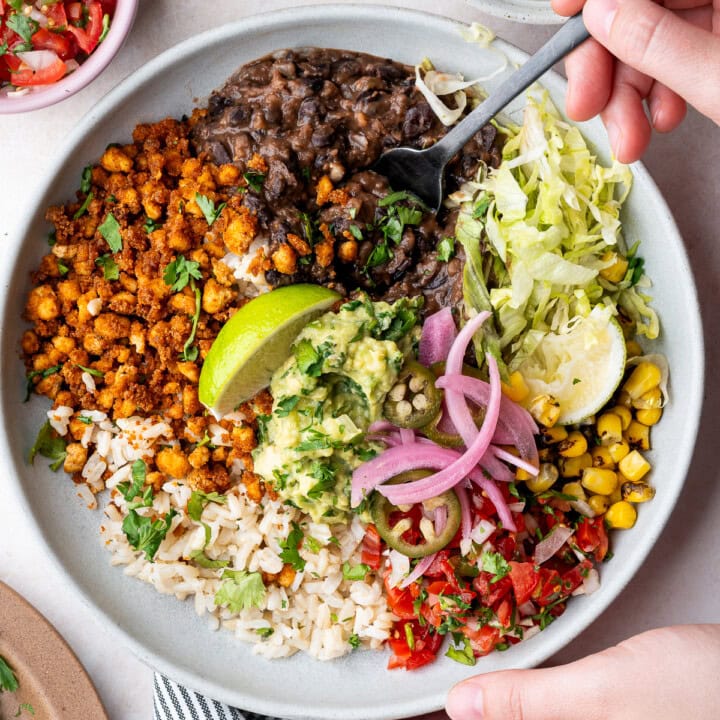 Vegan tofu burrito bowl with black beans, tofu crumbles, corn, pico de gallo, guacamole, and lime wedges