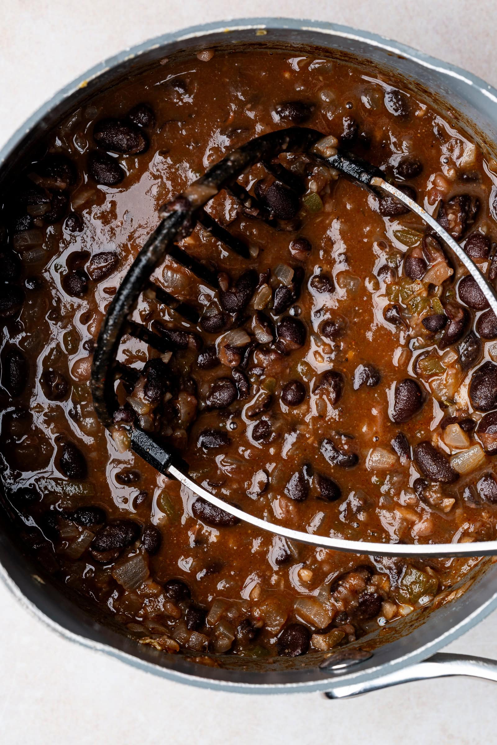 Black beans being mashed with a potato masher.