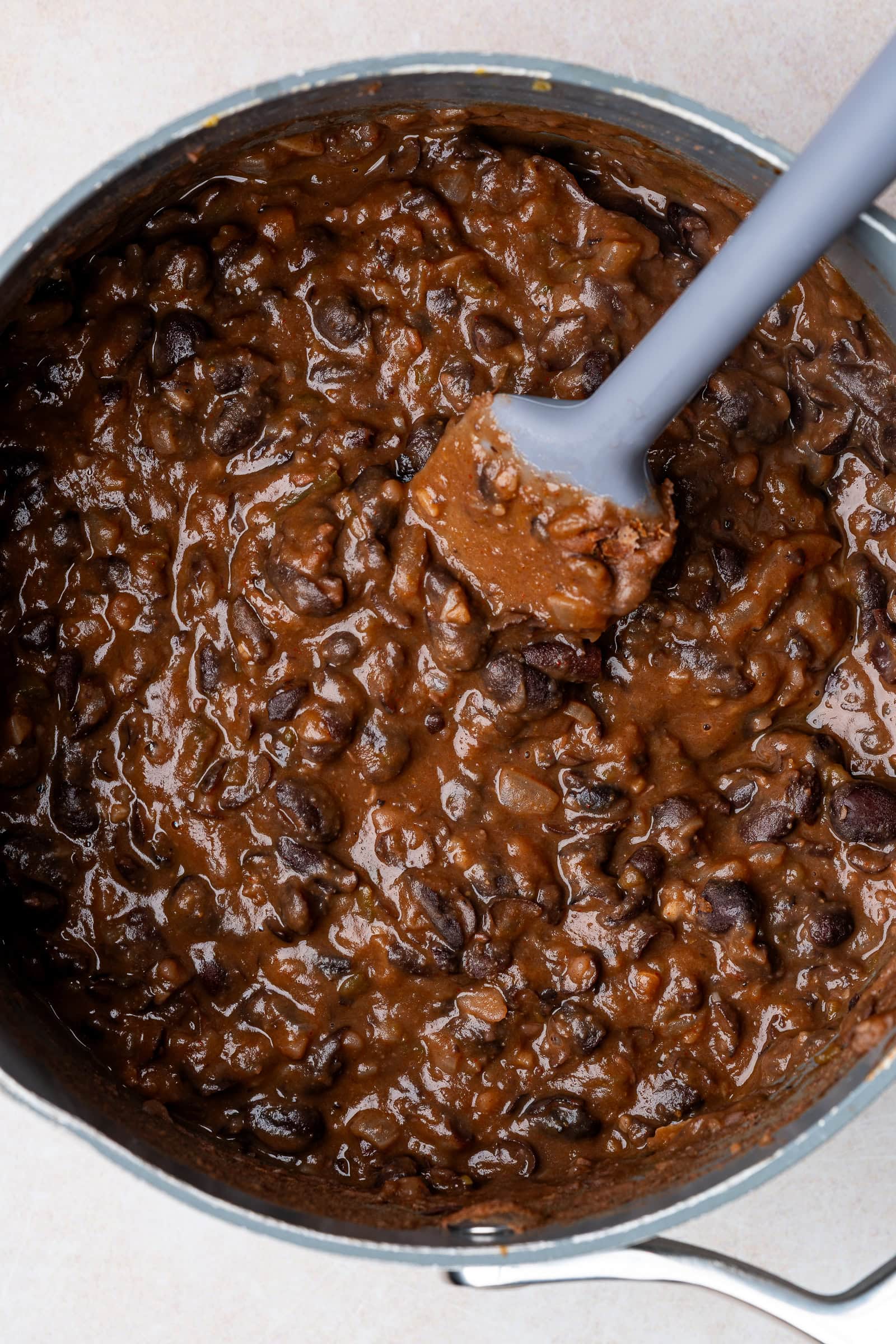 Cooked and mashed black beans in a small pot with a spatula.
