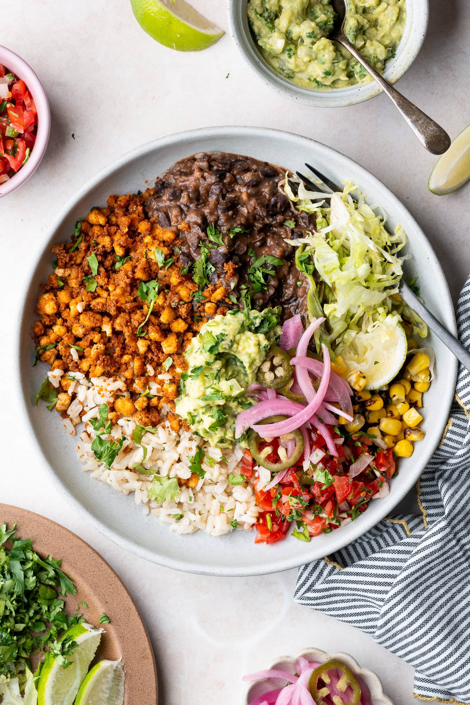 Vegan tofu burrito bowl with black beans, tofu crumbles, corn, pico de gallo, guacamole, and lime wedges