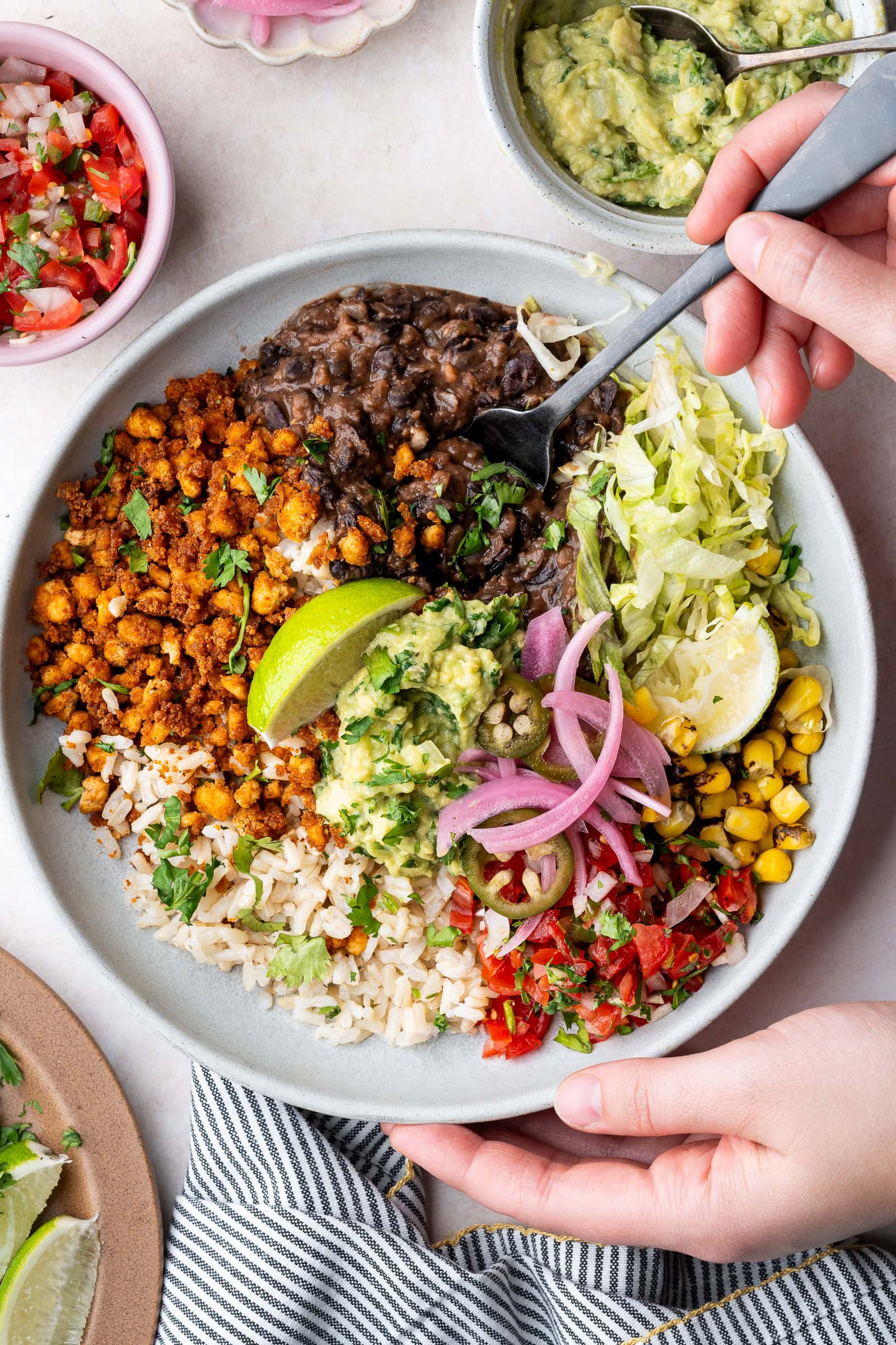 Hands holding a fork over a vegan tofu burrito bowl with black beans, tofu crumbles, corn, pico de gallo, and guacamole.