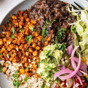 Vegan tofu burrito bowl with black beans, tofu crumbles, corn, pico de gallo, guacamole, and lime wedges