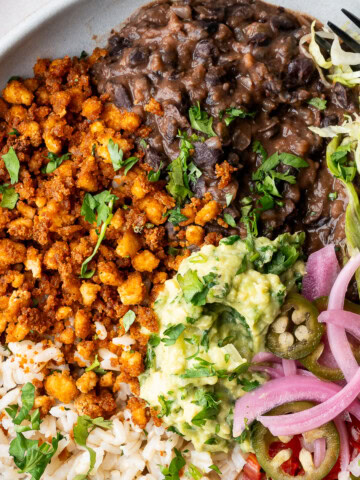 Vegan tofu burrito bowl with black beans, tofu crumbles, corn, pico de gallo, guacamole, and lime wedges