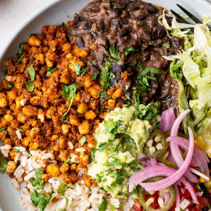 Vegan tofu burrito bowl with black beans, tofu crumbles, corn, pico de gallo, guacamole, and lime wedges