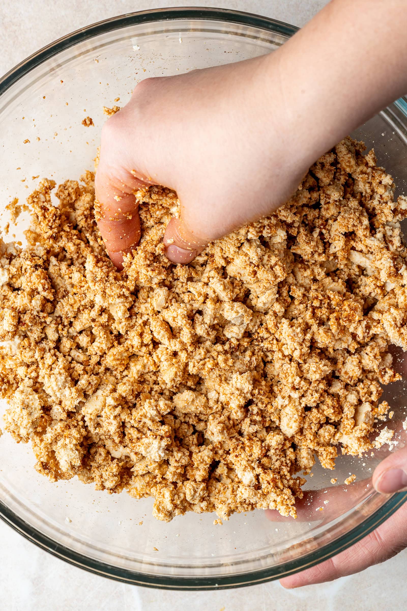 Clean hands crumbling the tofu and combining it with seasonings in glass bowl.