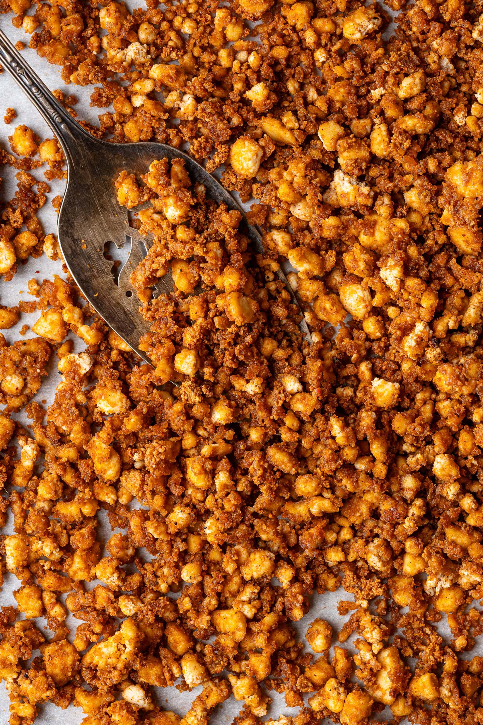 Crumbled tofu on a baking sheet being scooped with a spatula.