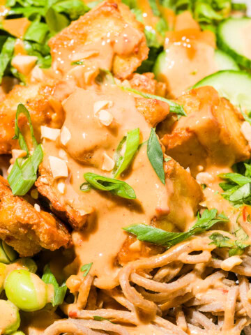 Close up of a drizzle of peanut sauce over crispy tofu noodle bowl.