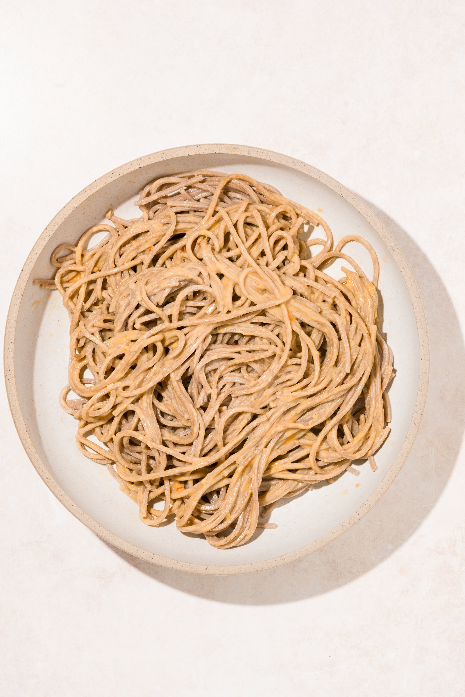 Soba noodles tossed with peanut sauce in shallow bowl.