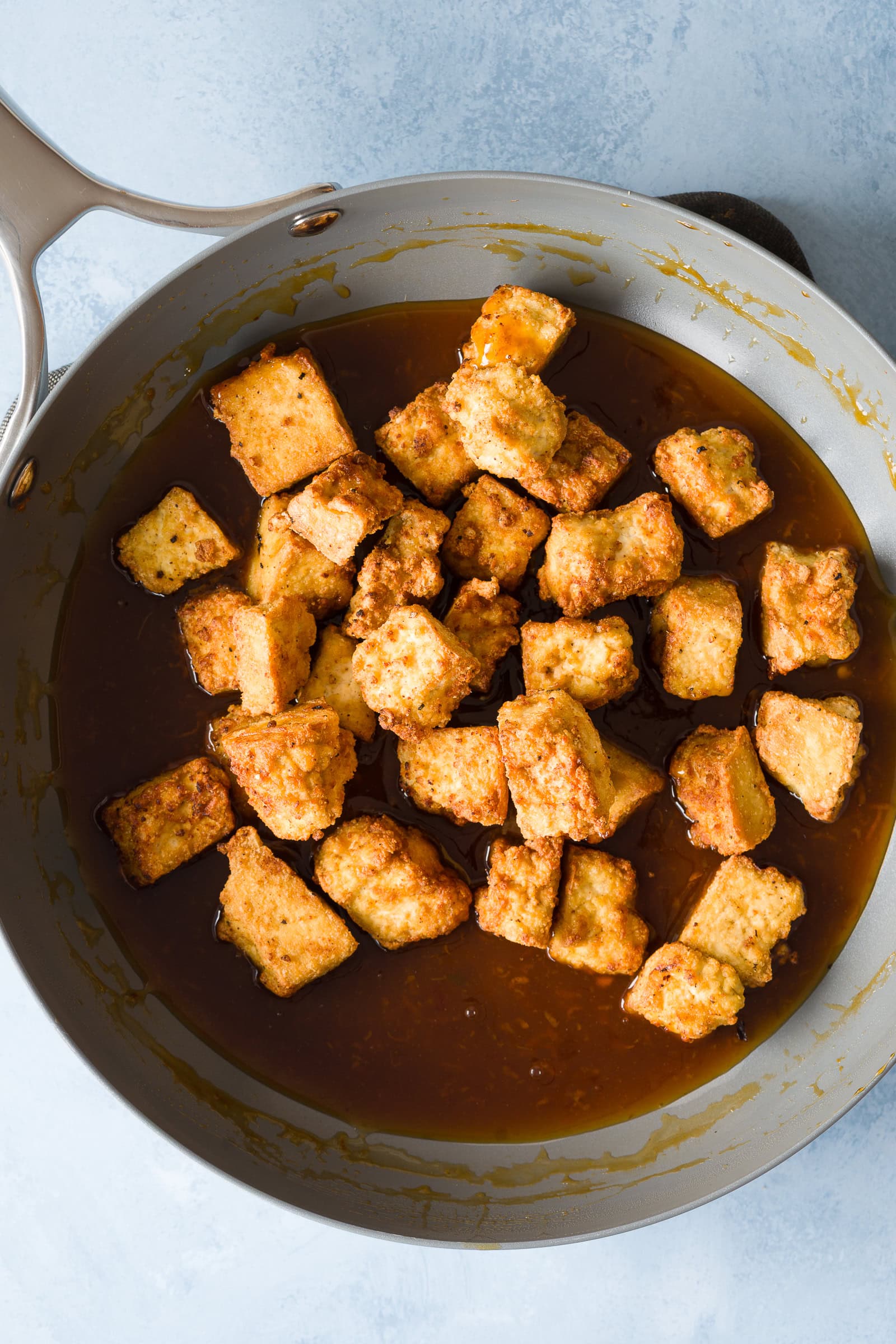 Tofu being tossed in sticky orange sauce.
