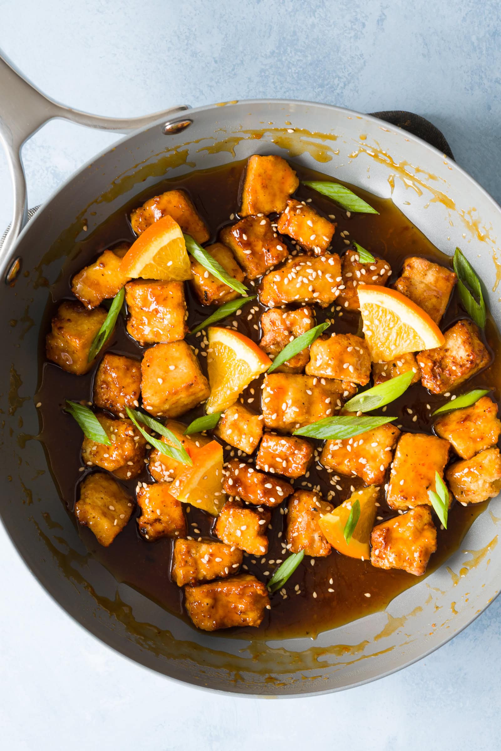 Crispy orange tofu in sticky sauce garnished with green onions, sesame seeds, and orange slices.