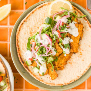 Vegan tofu shawarma with roasted onions and creamy yogurt tahini sauce topped with vegetables.