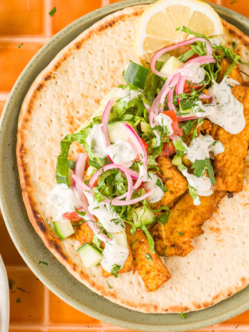 Vegan tofu shawarma with roasted onions and creamy yogurt tahini sauce topped with vegetables.