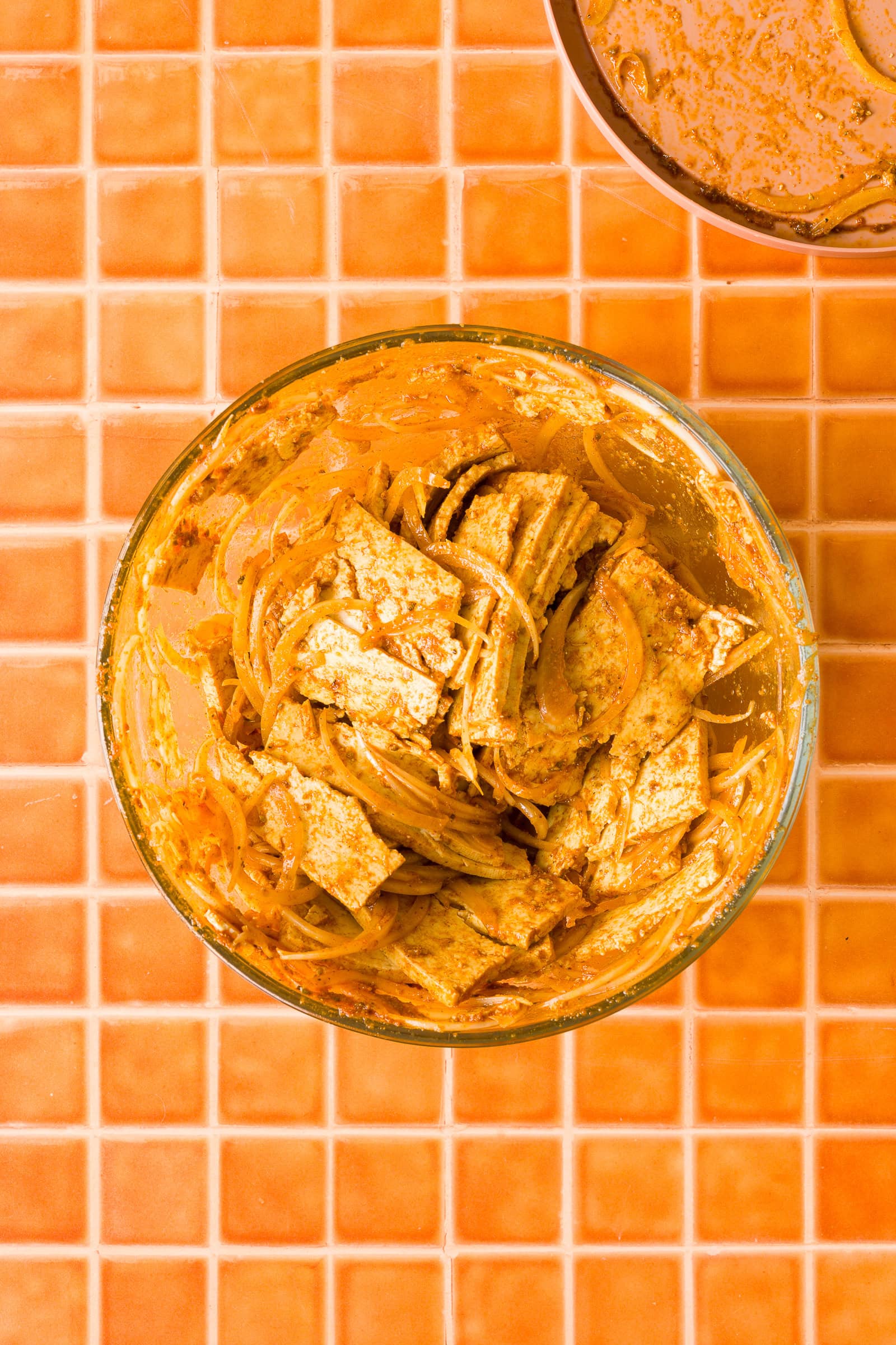 Tossing sliced tofu and onions until evenly coated in the shawarma marinade.