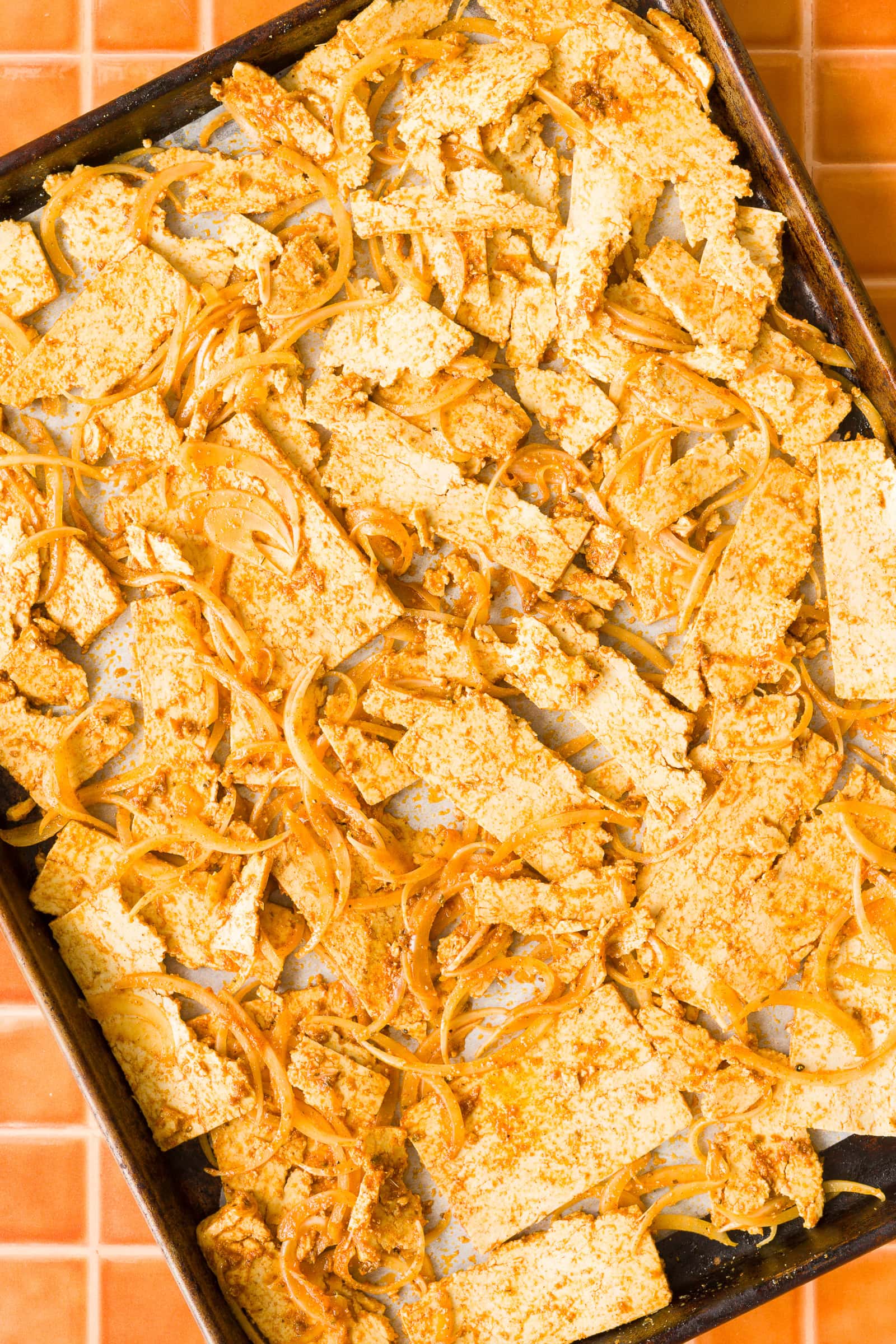 Marinated tofu and sliced onions spread on a baking sheet before roasting