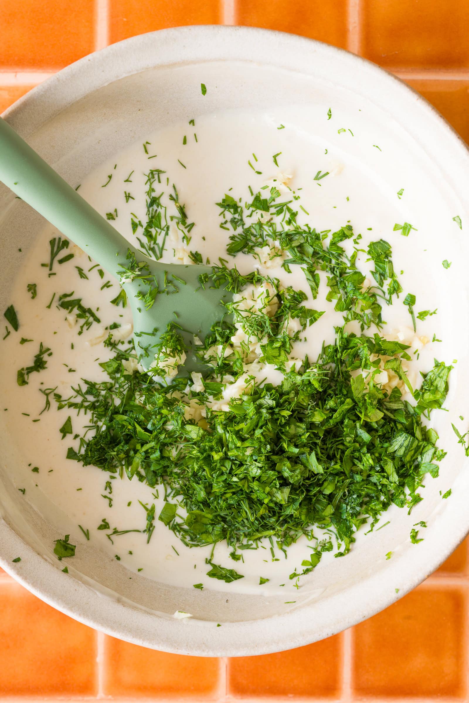 Vegan yogurt, tahini, lemon, garlic, and herbs in a bowl before mixing.