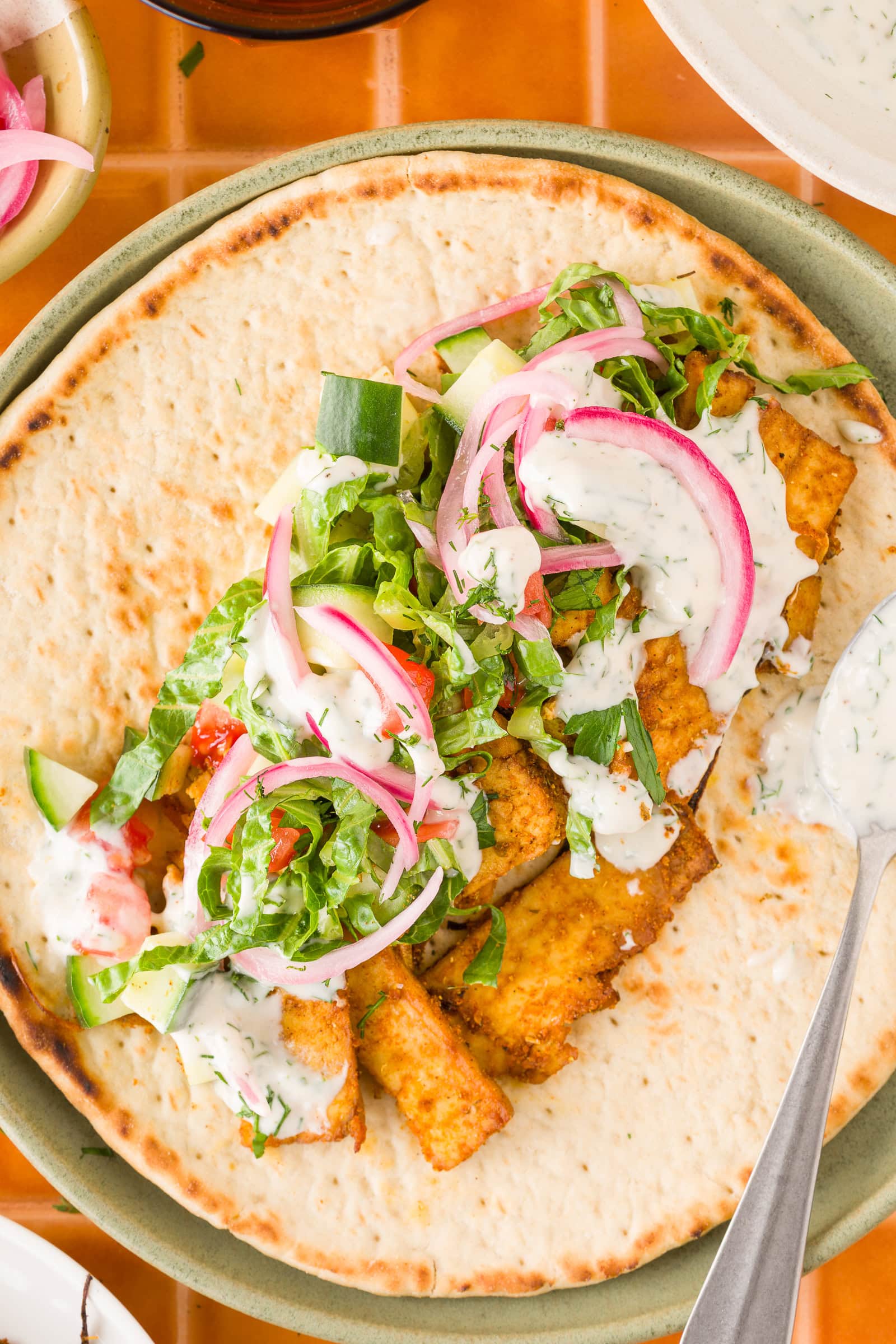 Close up of tofu shawarma served on flatbread with lettuce, tomatoes, cucumber, pickled onions, and yogurt sauce.