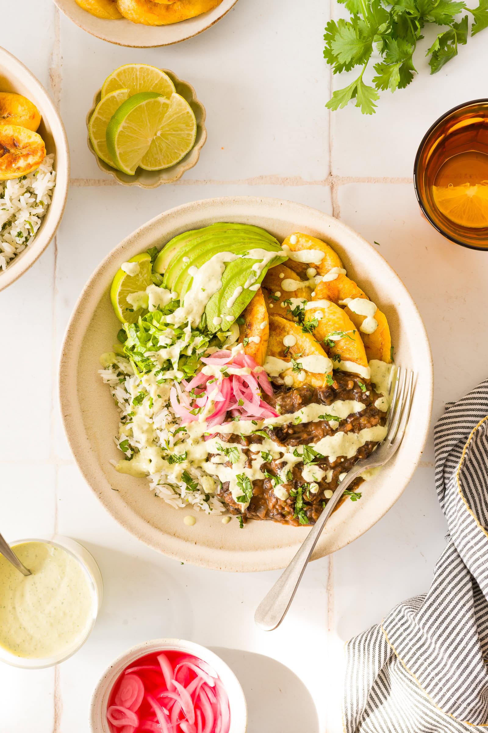 Black bean plantain bowl with cilantro lime rice, avocado, lettuce, pickled red onions, and creamy cilantro lime sauce.