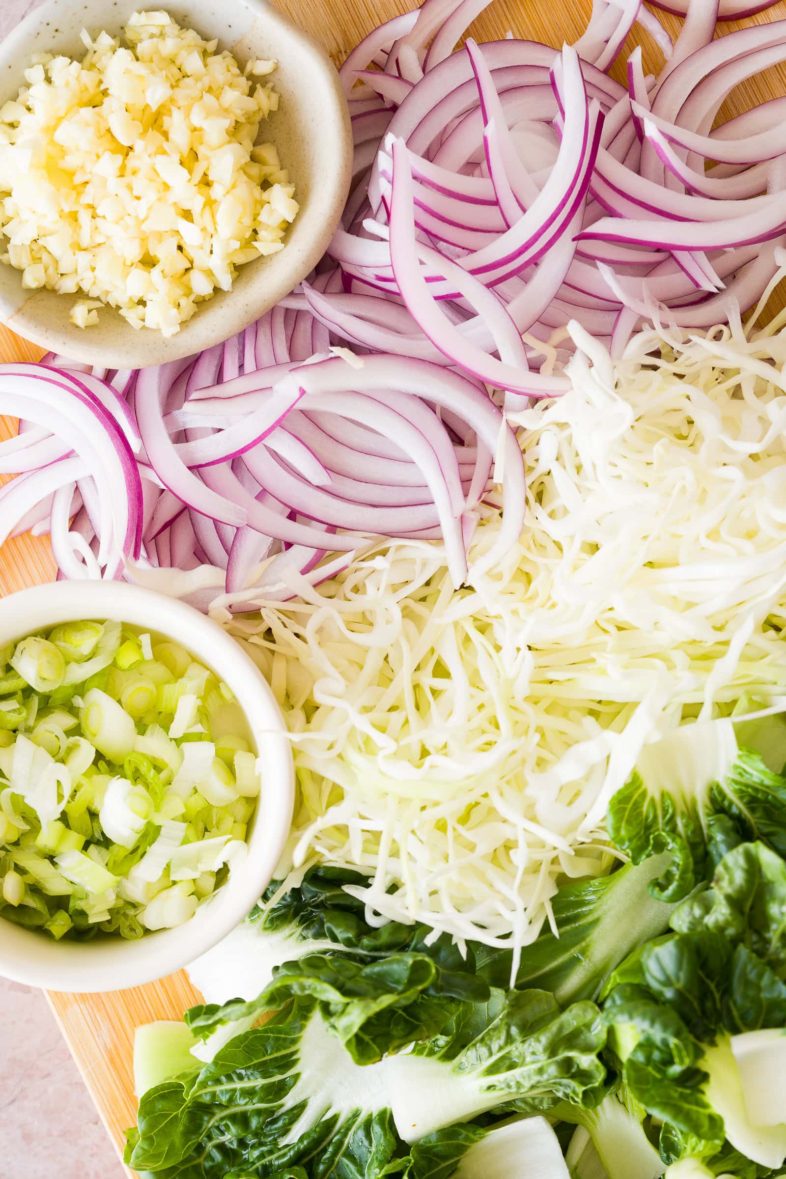 Chopped cabbage, bok choy, red onion, garlic and green onions on a cutting board.