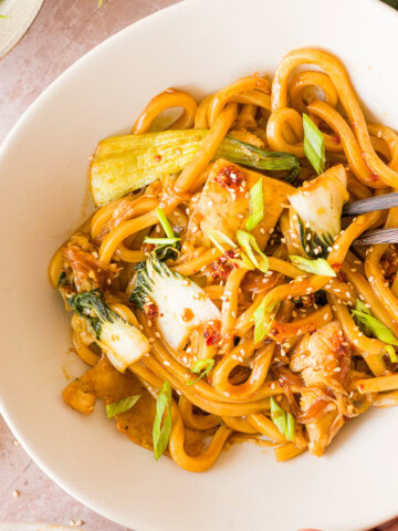 Close up chili garlic noodles in a bowl with green onions and sesame seeds.