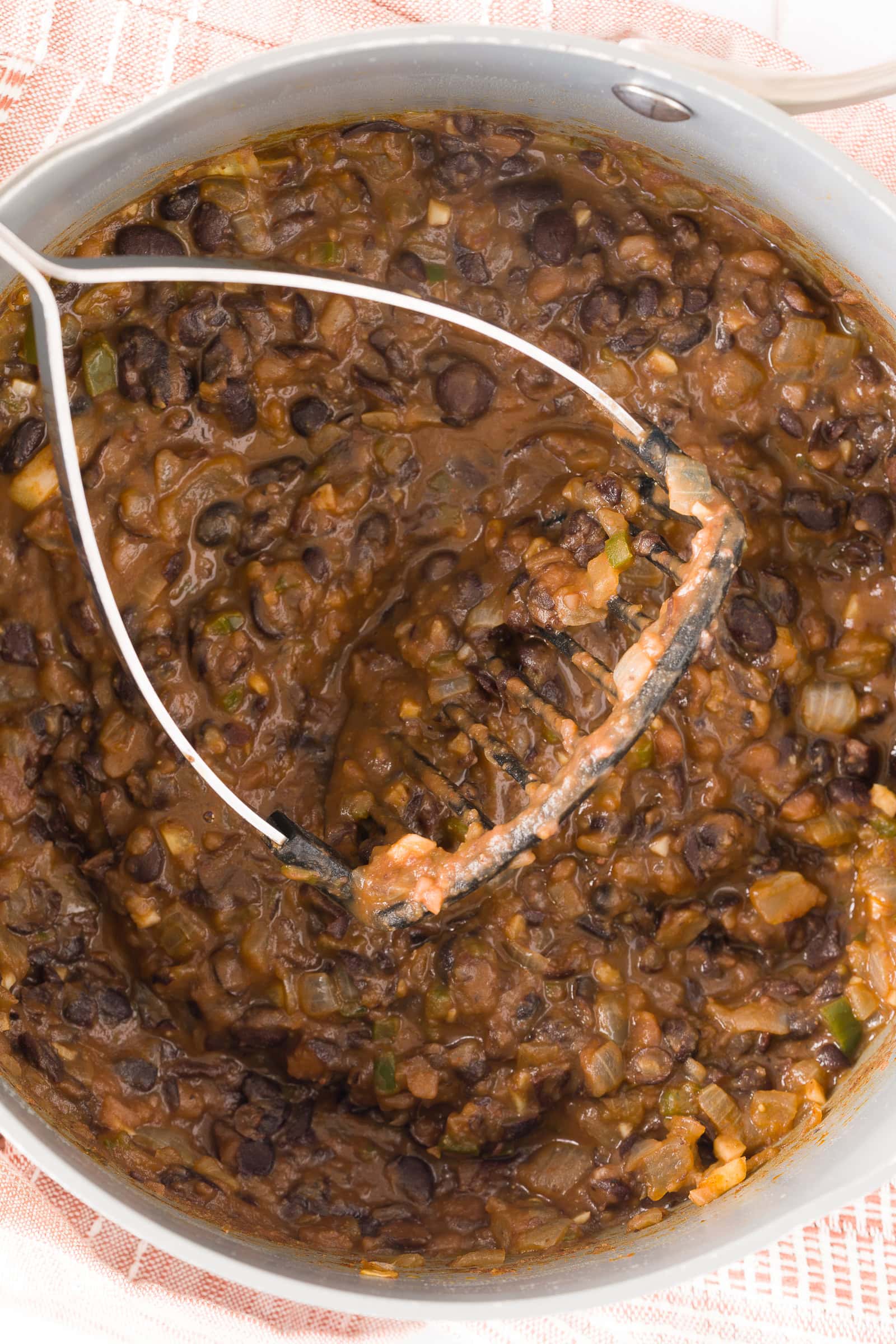 Simmered black bean being mashed in a pan.
