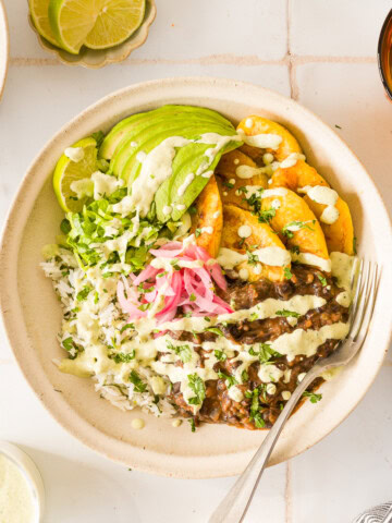 Close-up of caramelized plantains and black beans over rice with avocado, pickled red onions, corn, and jalapeño sauce.
