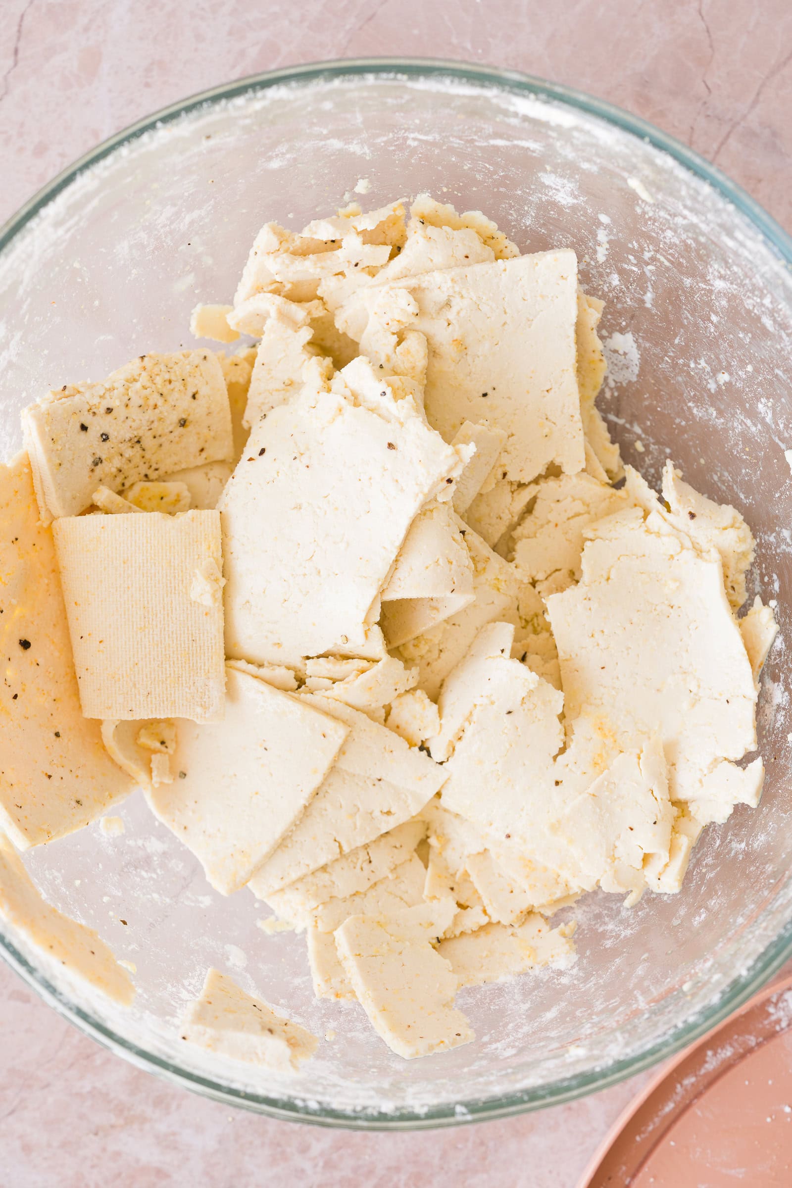 Thinly shaved tofu tossed with cornstarch and seasonings in a bowl.