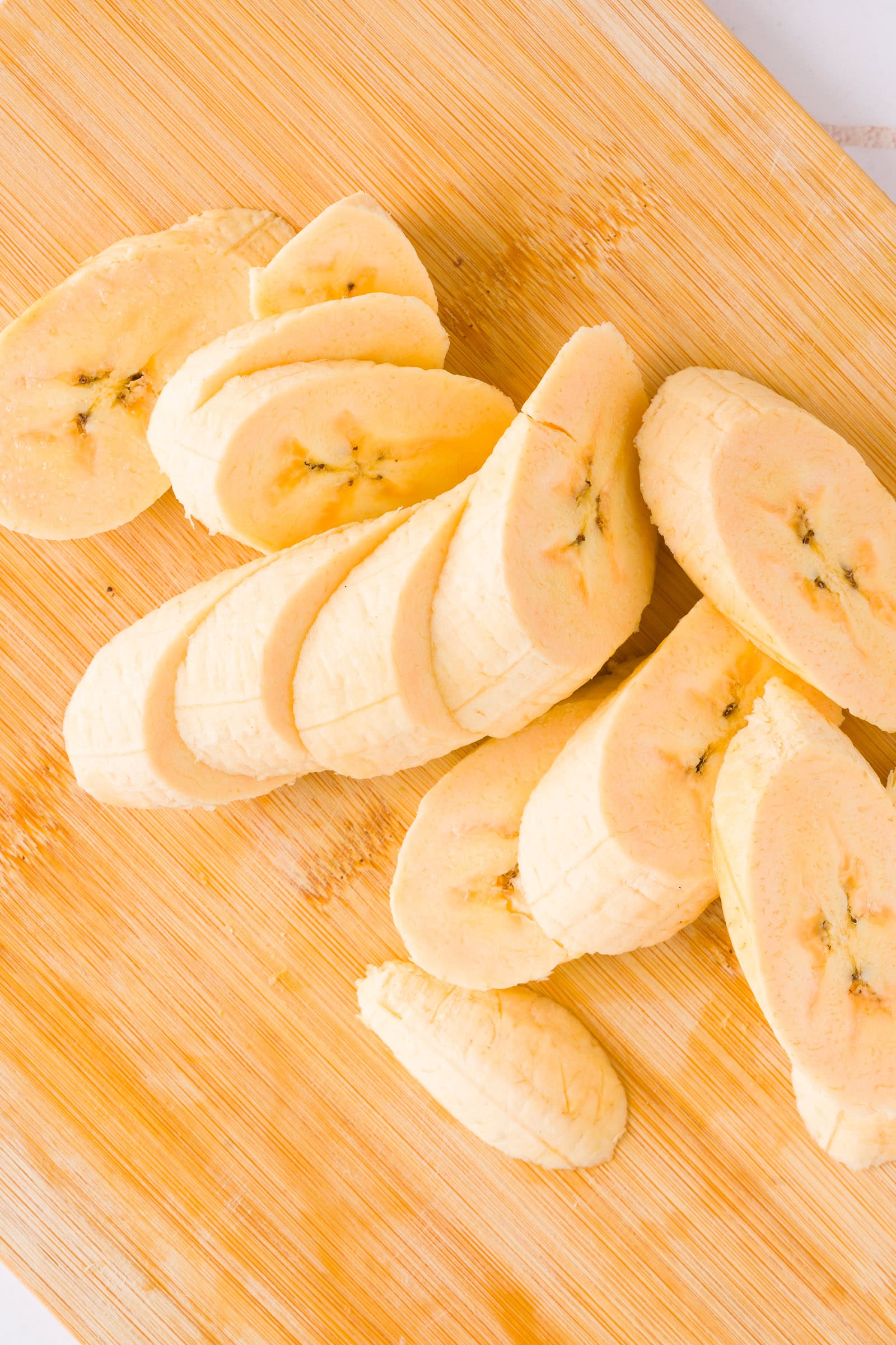 Plantains sliced diagonally on a wooden cutting board
