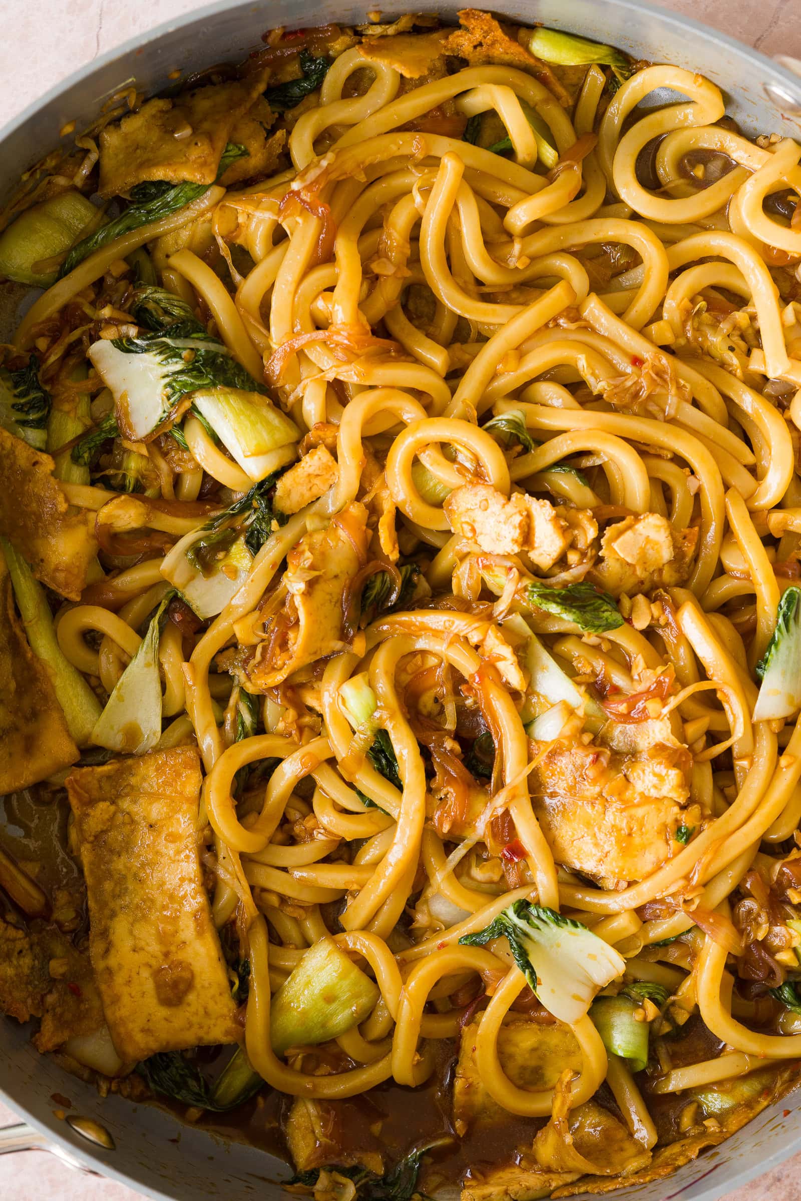 Chili garlic udon noodles with tofu and vegetables tossed together in a frying pan.