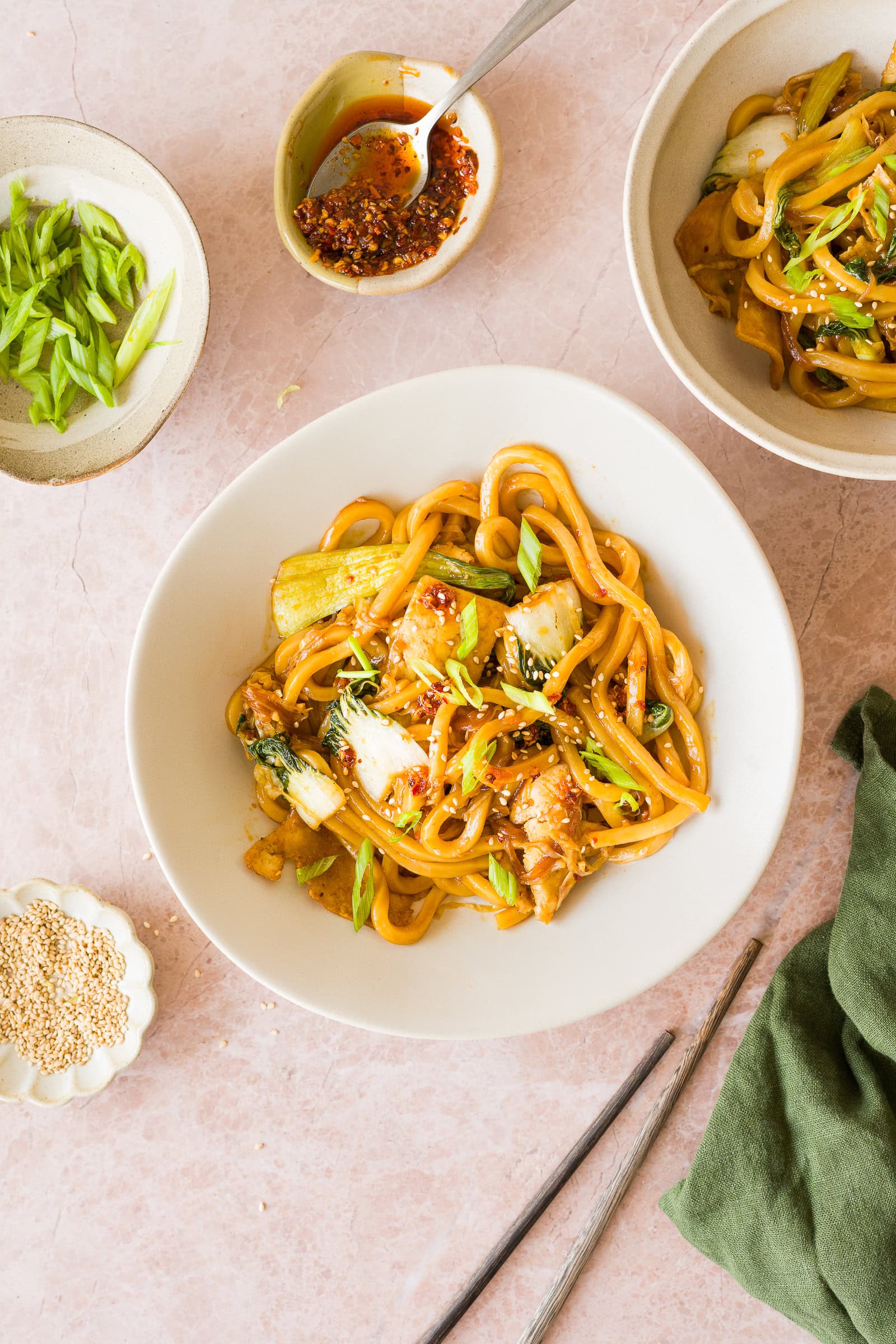 Vegan udon noodles with crispy tofu and vegetables in serving bowl garnished with green onions.